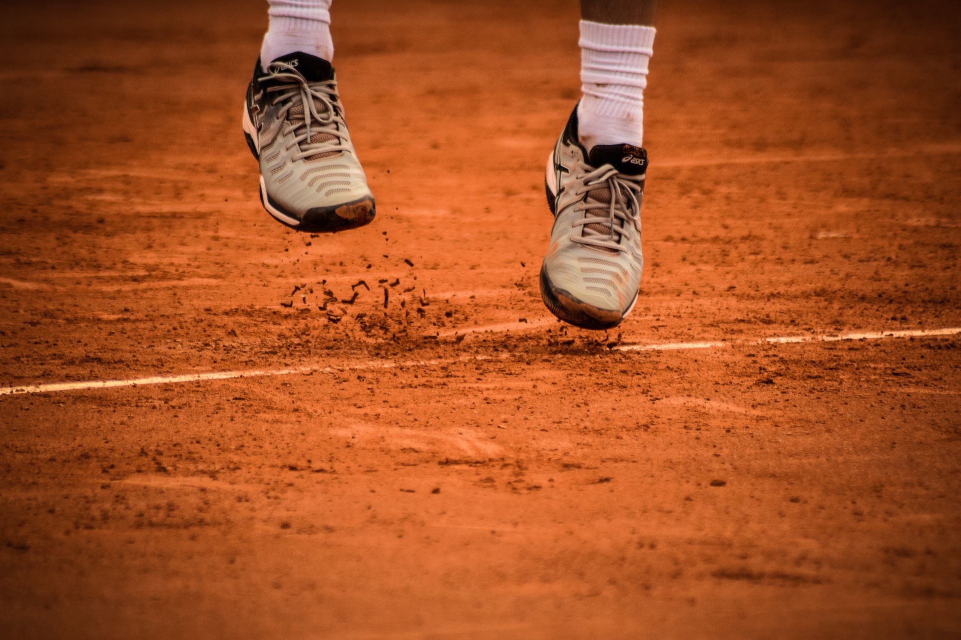 ASICS tennis shoes jumping on a clay court